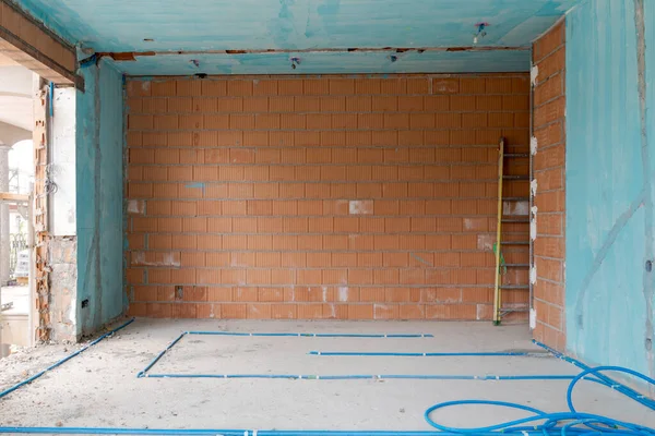 Interior of an ancient villa under renovation with blue painted walls, electrical pipes on the ground and freshly laid orange bricks. Nobody inside