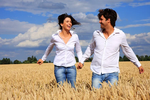 Glückliches Paar läuft lächelnd auf einem Feld und hält Händchen unter blauem Himmel Stockbild