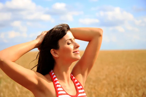 güzel bir kadın arka plan buğday alan üzerinde güneşin tadını çıkarıyor