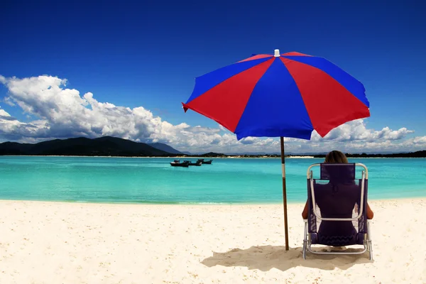 beyaz kumlu plaj renkli güneş şemsiyesi altında oturan kadın