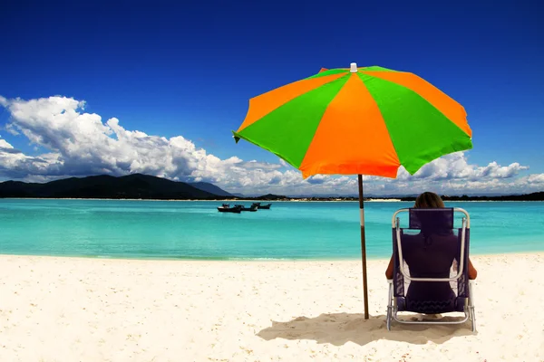 beyaz kumlu plaj renkli güneş şemsiyesi altında oturan kadın