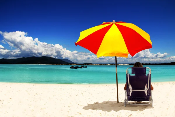 beyaz kumlu plaj renkli güneş şemsiyesi altında oturan kadın