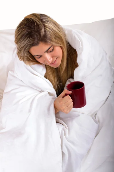 マグカップを保持している白い毛布の下で若い女性 ストック画像