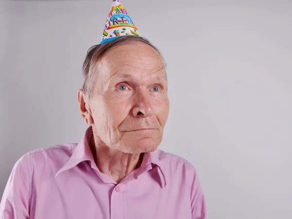 Porträt eines alten Mannes mit lustigem Gesicht und Happy Birthday Papierhut auf grauem Hintergrund — Stockfoto