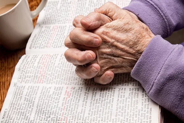 Mains de femme aînée sur la Bible Images De Stock Libres De Droits