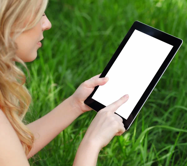 Menina detém um tablet em um fundo de grama verde — Fotografia de Stock