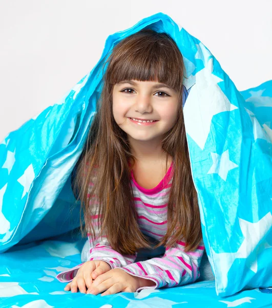 Linda menina deitada na cama sob um cobertor azul — Fotografia de Stock