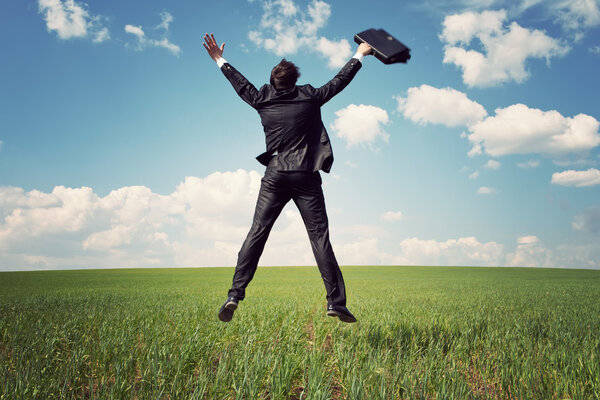 businessman in suit jumping in field and holding the bag