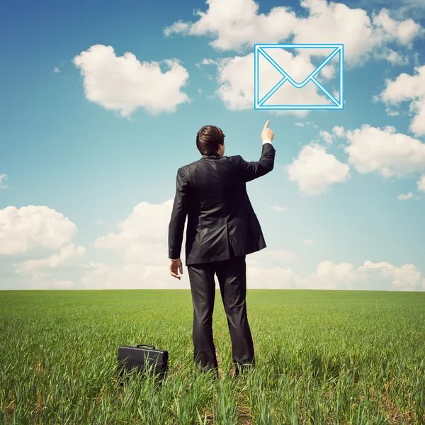 Бизнесмен, стоящий в поле и указывающий пальцем на почту — стоковое фото