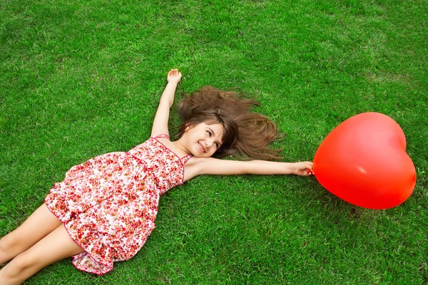 Schönes Mädchen, das auf dem Rasen liegt und einen roten Ball in der Hand hält — Stockfoto