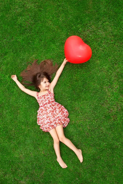 Hermosa chica acostada en la hierba y sosteniendo una bola roja en el — Foto de Stock