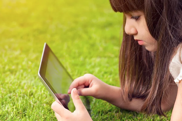 Little girl lying on grass and touches the screen a tablet — Stock Photo, Image