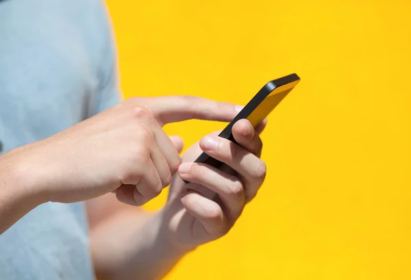 Jongen holding een telefoon en een touchscreen tegen een gele muur — Stockfoto