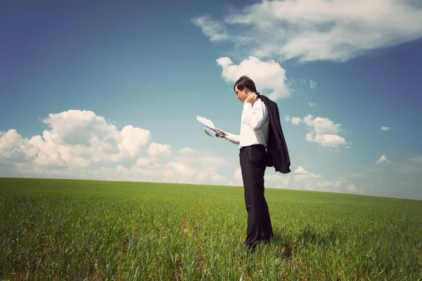 Geschäftsmann steht auf einem Feld mit blauem Himmel und liest die — Stockfoto