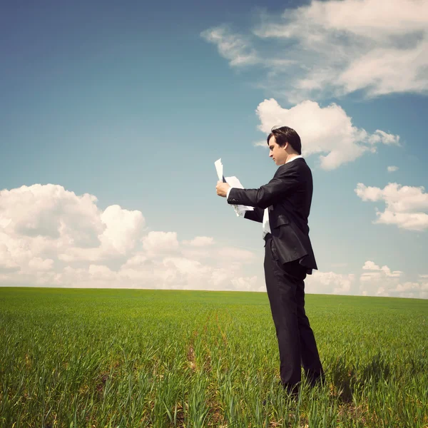 Hombre de negocios de pie en un campo con un cielo azul y lee el ne —  Fotos de Stock