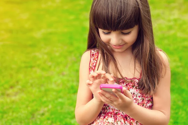 Mooi meisje houdt van een telefoon op een achtergrond van groen gras — Stockfoto