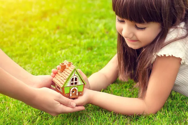 Little girl and a woman hands holding small house on a backgroun — Stock Photo, Image