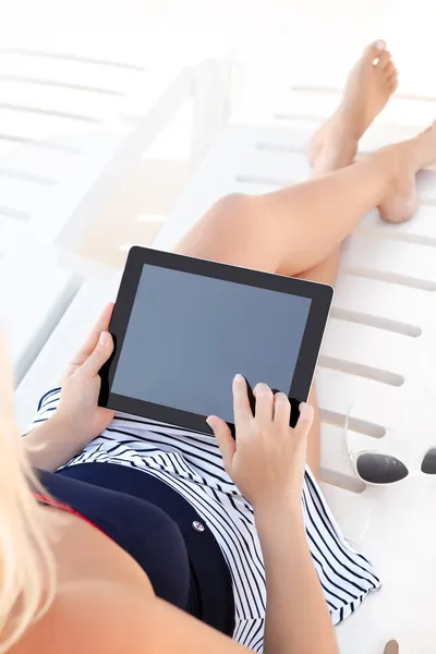 girl in a bathing suit lying on a white chaise lounge with a tab