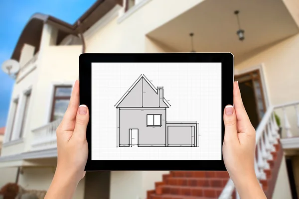 Female hands hold a tablet with drawing of apartment house on th — Stock Photo, Image