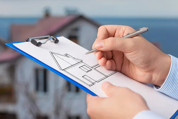 Empresário desenha um desenho de uma casa no fundo de um — Fotografia de Stock