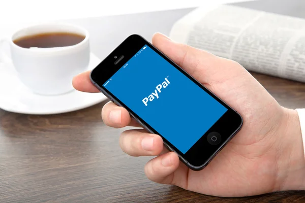 Mano masculina sosteniendo un iPhone con aplicación PayPal en una pantalla — Foto de Stock
