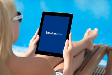 Girl lying by the pool and holding ipad with Booking on the scre