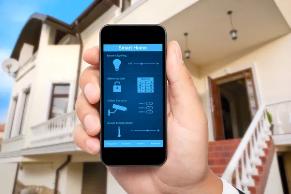 Mano maschile tenere un telefono con sistema smart house sullo sfondo — Foto Stock