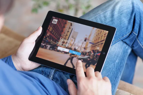 Man sitting on the sofa and holding iPad with App LinkedIn on th — Stock Photo, Image