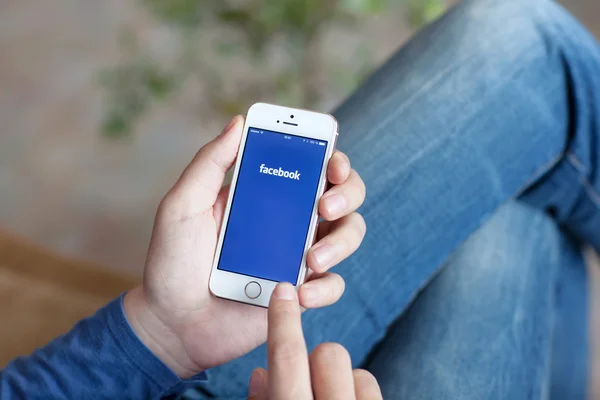 Uomo in possesso di un iPhone bianco con App Facebook sullo schermo — Foto Stock