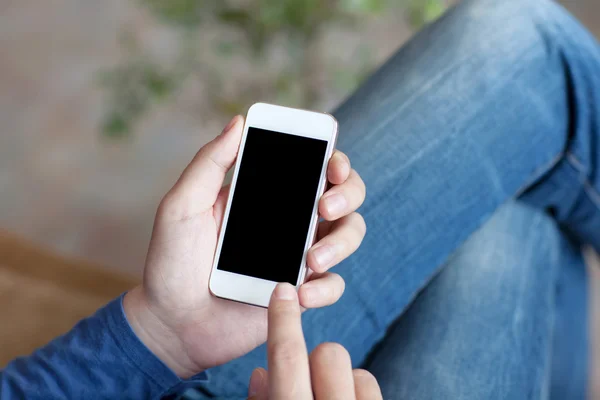 Man sitting on a sofa and holding a white touch phone with a bla — Stock Photo, Image