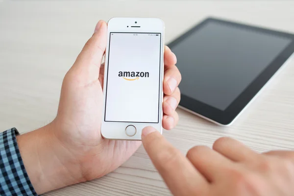 Seseorang memegang iPhone 5s putih dengan aplikasi Amazon di layar atas — Stok Foto