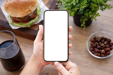 Kadın eli, kafeteryada burger masası olan bir telefon tutuyor. 