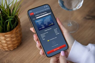 Kafe 'deki masanın üstündeki ekranda internetten alışveriş uygulaması olan kadın elleri telefonu tutuyor. 