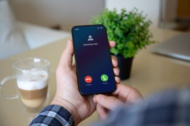 Erkek, elinde altın bir telefon, ofiste ekrandan gelen arama var. 