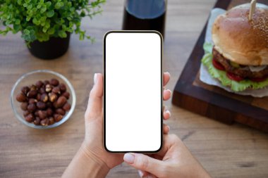 female hands hold phone with isolated screen background of burger in cafe