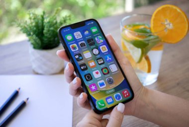 Alanya, Turkey - July 28, 2022: Woman hand holding iPhone 13 with home screen IOS 16 on the screen.