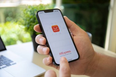 Alanya, Türkiye - 28 Nisan 2022: İnternet üzerinden alışveriş hizmeti Aliexpress ile iPhone 13 'ü tutan adam ekranda.