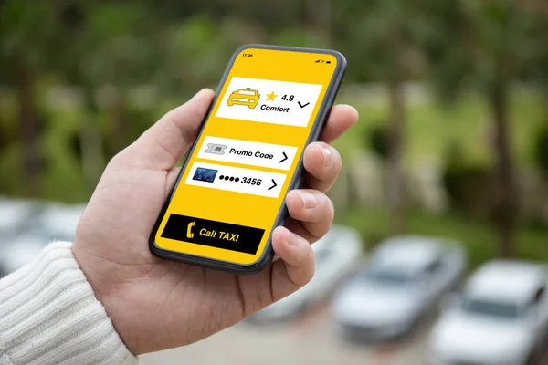 男子手持电话与应用程序出租车在屏幕上的背景白色汽车在停车场 — 图库照片