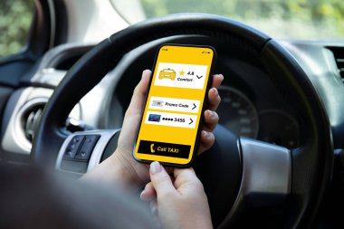 Kadın elleri, arabadaki direksiyonun arka planında uygulamalı çağrı taksisiyle telefonu tutuyor.