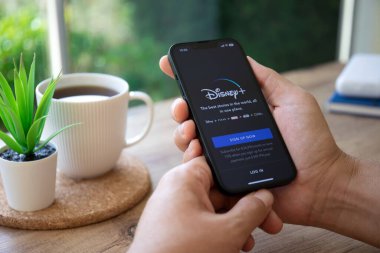 Alanya, Türkiye - 29 Eylül 2022: Apple iPhone 14 'ü çok uluslu eğlence şirketi Disney ile tutan adam ekranda yayın yapan medya ve video sağlıyor.