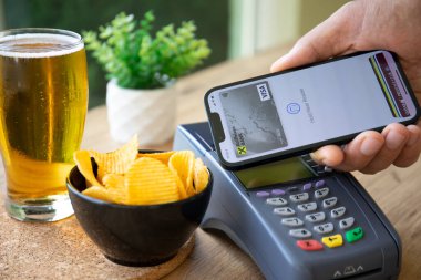 Alanya, Türkiye - 4 Ekim 2022: Ekranda Raiffeisenbank uygulamalı iPhone 14 ile el ele tutuşan ve internetten POS terminali üzerinden ödeme yapan adam kafede bira satın aldı