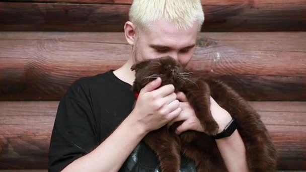 Um jovem beija seu gato satisfeito enquanto o segura em seus braços — Vídeo de Stock