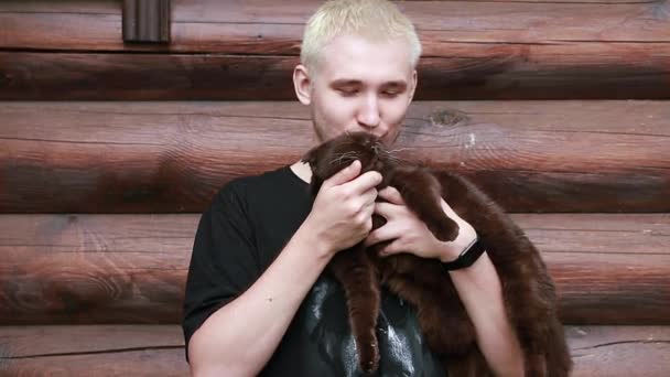 Um jovem beija seu gato satisfeito enquanto o segura em seus braços — Vídeo de Stock