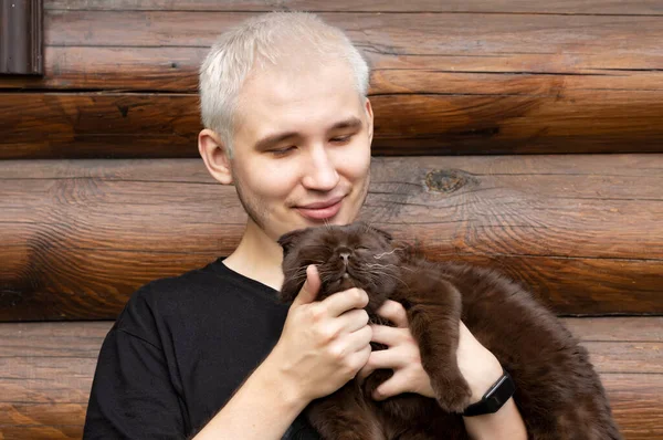 A young guy strokes the neck of his contented cat, holding him in his arms — Stockfoto