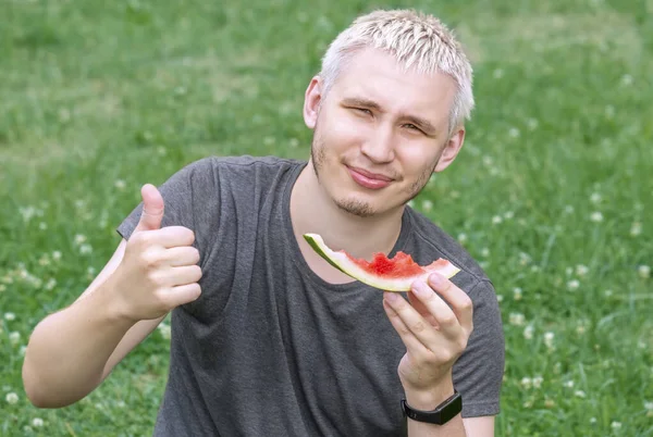 Der Typ isst eine Wassermelone, die auf dem grünen Rasen sitzt — Stockfoto