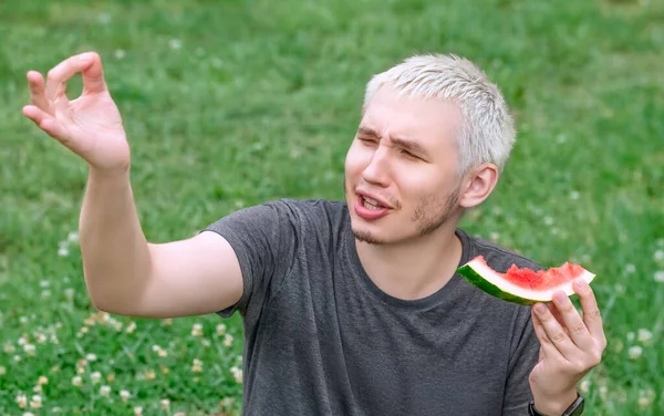 Der Typ isst eine Wassermelone, die auf dem grünen Rasen sitzt — Stockfoto