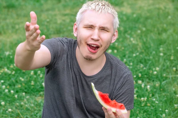Der Typ isst eine Wassermelone, die auf dem grünen Rasen sitzt — Stockfoto