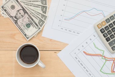 İş konsepti: Dolar banknotları, grafik, hesap makinesi ve ahşap masadaki kahve..