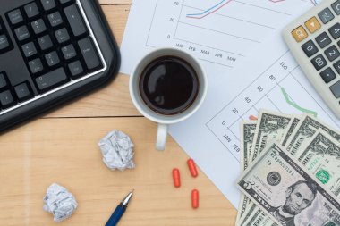 Klavye, dolar, grafik, hesap makinesi, ilaç, kalem ve kahveli işyeri.