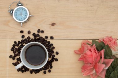 Çalar saat, kahve ve çiçekler ahşap masada..